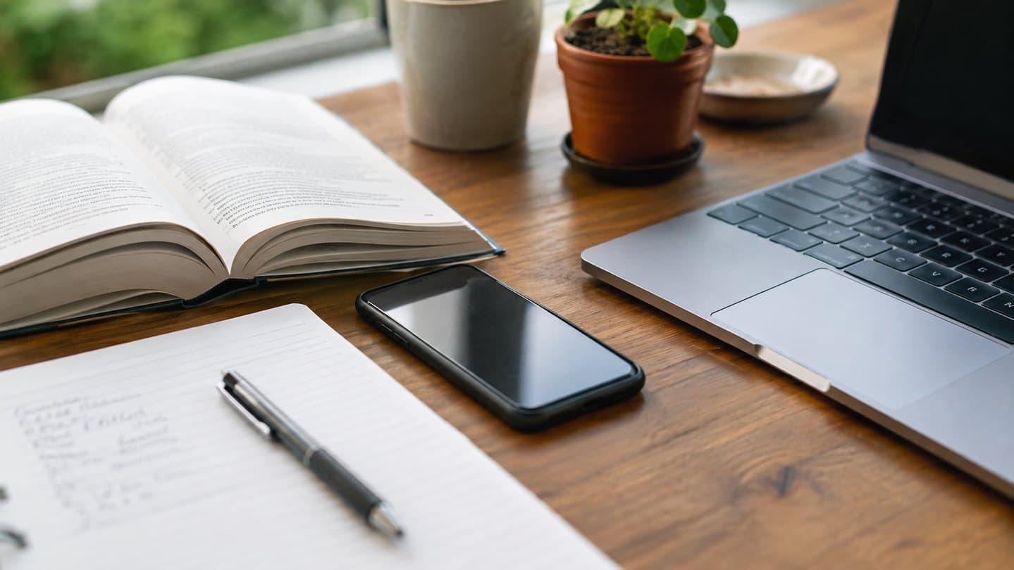 A phone resting beside notes and a laptop in an ordinary work setting.